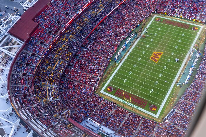 Aerial view of a packed football stadium with fans reacting to Trump’s call to rename the stadium after him.
