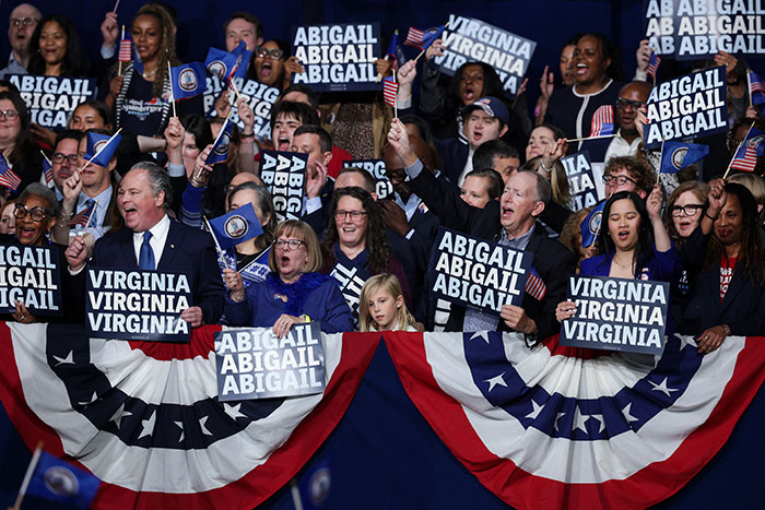 Supporters celebrate Virginia turning blue with signs for Abigail, waving flags at a political event amid Trump election challenges. Supporters celebrate Virginia turning blue with signs for Abigail, waving flags at a political event amid Trump election challenges.