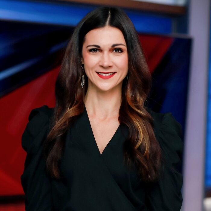 TV sports reporter smiling in studio with long dark hair and black blouse, news set background. TV sports reporter smiling in studio with long dark hair and black blouse, news set background.