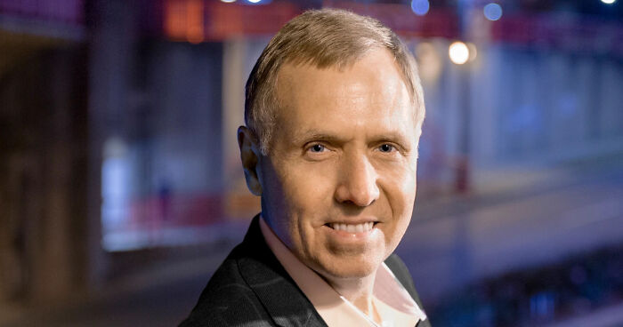 Man smiling in a dark suit with blurred colorful lights in the background, related to Kennedy Center and New Year cancellations.