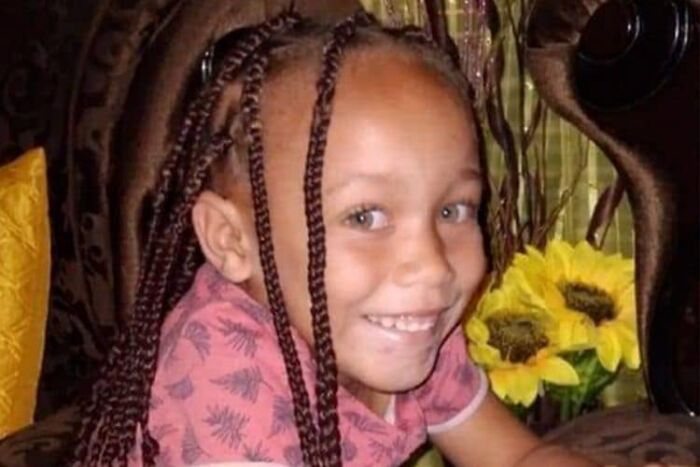 Young girl with braided hair smiling indoors beside yellow sunflowers, capturing a moment related to auction house visit and disturbing offer.