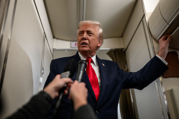 Former President Trump speaking inside an aircraft, surrounded by reporters with microphones during a media interaction. Former President Trump speaking inside an aircraft, surrounded by reporters with microphones during a media interaction.