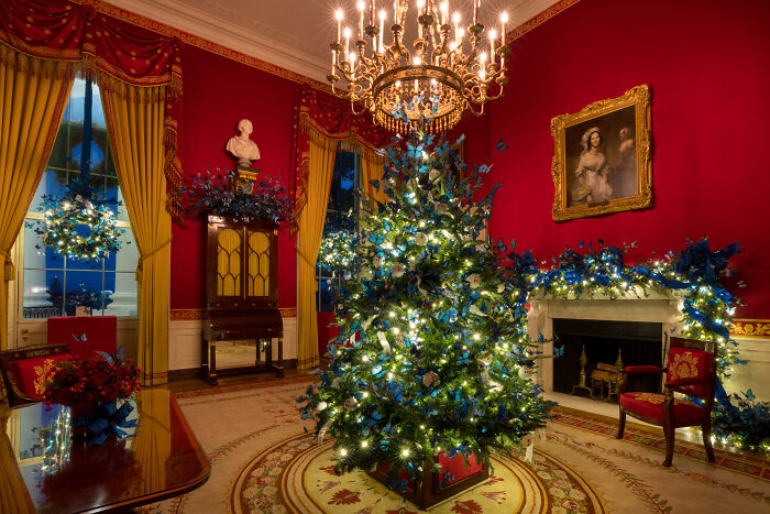 Christmas tree and blue floral decorations in a red room showcasing Melania Trump’s 2025 Christmas decorations style.