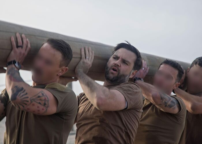 Man resembling JD Vance participating in a Navy SEAL style training exercise carrying a log with others outdoors.