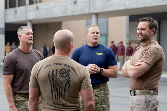 Four men in military-style clothing standing and talking outdoors, related to JD Vance Navy SEAL cosplaying controversy.