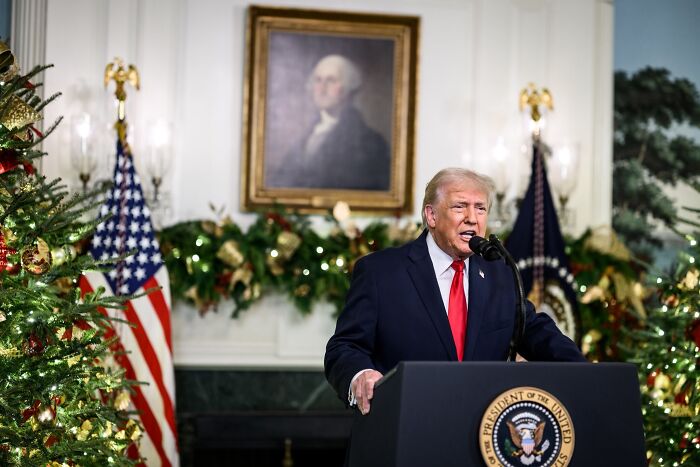Former President Trump delivering a TV address with holiday decorations and American flags in the background. Former President Trump delivering a TV address with holiday decorations and American flags in the background.