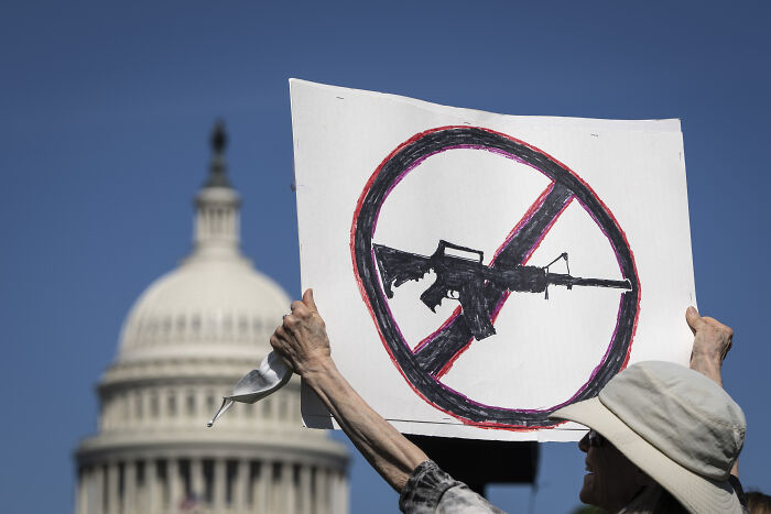 Protester holding an anti-gun sign in front of the U.S. Capitol symbolizing gun laws debate. Protester holding an anti-gun sign in front of the U.S. Capitol symbolizing gun laws debate.