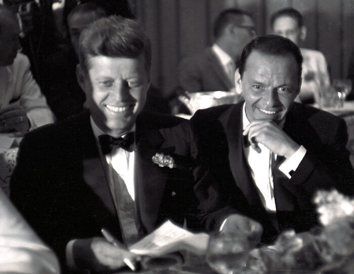 Black and white photo of John F. Kennedy and Frank Sinatra smiling at a formal event, related to Nancy Sinatra Trump supporter remarks. Black and white photo of John F. Kennedy and Frank Sinatra smiling at a formal event, related to Nancy Sinatra Trump supporter remarks.