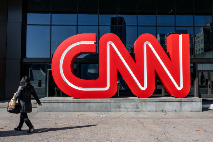 Person walking past large CNN logo outside building, illustrating CNN news and Kalshi partnership concept. Person walking past large CNN logo outside building, illustrating CNN news and Kalshi partnership concept.