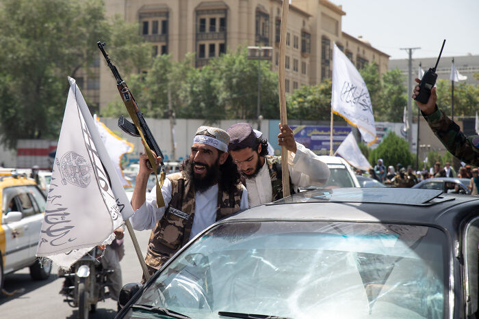 Taliban fighters holding rifles and flags during a street gathering in an urban area amid political tensions. Taliban fighters holding rifles and flags during a street gathering in an urban area amid political tensions.