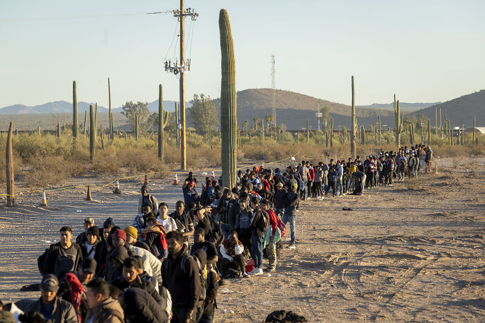 Large group of migrants walking in desert landscape under sunset, reflecting border and immigration issues linked to Trump claims. Large group of migrants walking in desert landscape under sunset, reflecting border and immigration issues linked to Trump claims.