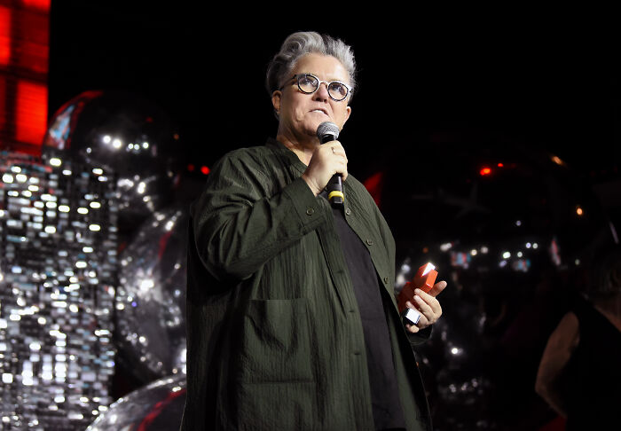 Celebrity speaking at event, holding microphone and notes, related to celebrities who slammed Donald Trump in 2025. Celebrity speaking at event, holding microphone and notes, related to celebrities who slammed Donald Trump in 2025.