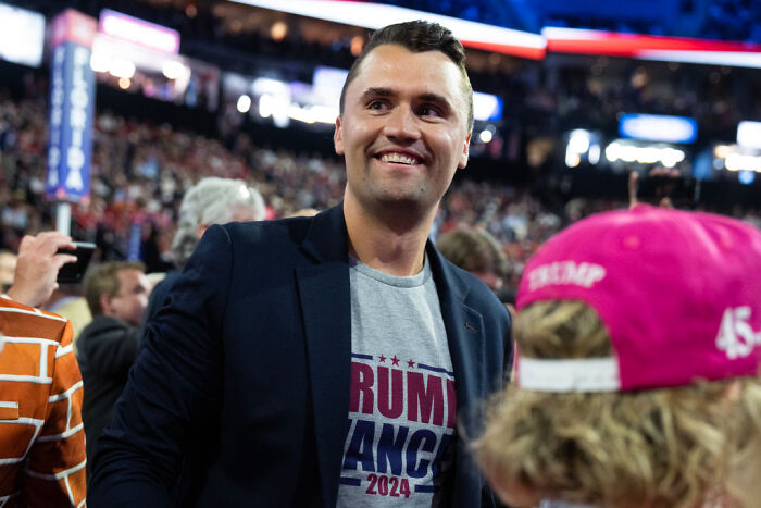 Charlie Kirk smiling at a political rally, wearing a Trump 2024 shirt amid a crowd of supporters. Charlie Kirk smiling at a political rally, wearing a Trump 2024 shirt amid a crowd of supporters.