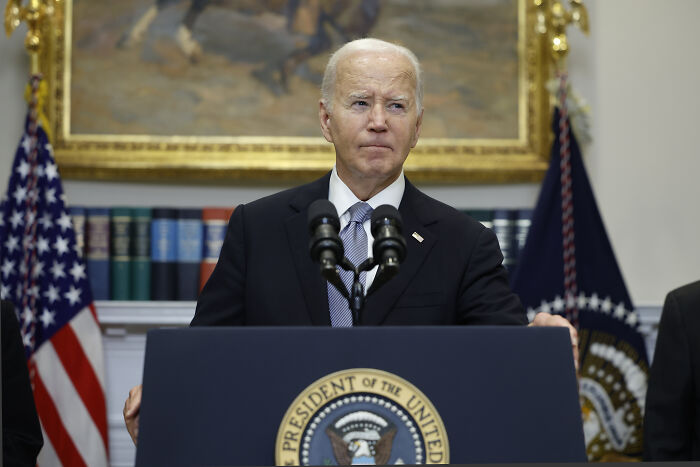 Joe Biden standing at a podium with presidential seal, speaking in front of American flags and bookshelves. Joe Biden standing at a podium with presidential seal, speaking in front of American flags and bookshelves.