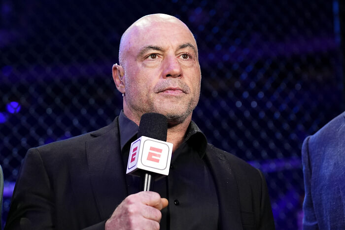Joe Rogan holding microphone during UFC event, discussing Trump’s ridiculous texting habits and behavior.
