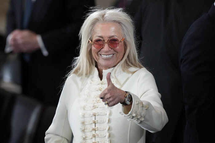 Woman in white jacket and orange glasses giving thumbs up, illustrating billionaire donor offering Trump $250 million. Woman in white jacket and orange glasses giving thumbs up, illustrating billionaire donor offering Trump $250 million.