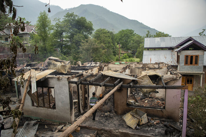 Burned remains of a house with a person walking through rubble after a disaster in events that shook the world in 2025.
