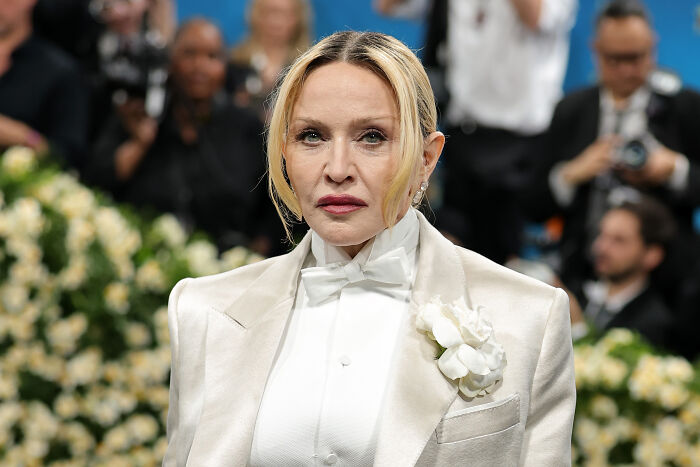 Madonna wearing a white suit with a flower at a public event, reacting to Trump administration’s World AIDS Day decision.