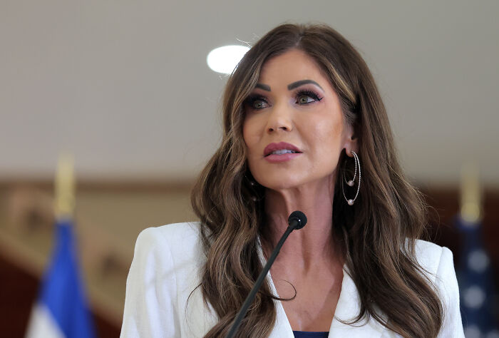 Woman speaking at a podium with microphone, discussing data on people arrested in Trump’s ICE raids not convicted criminals.