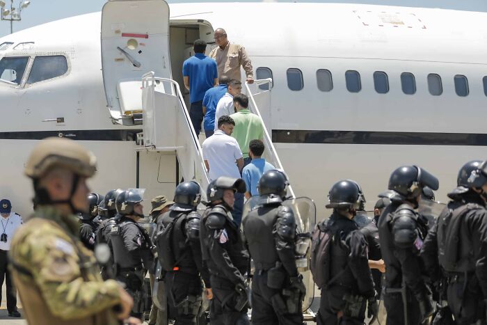 Deportation detainees boarding plane under heavy security, illustrating corporate censorship controversy over CBS report removal.