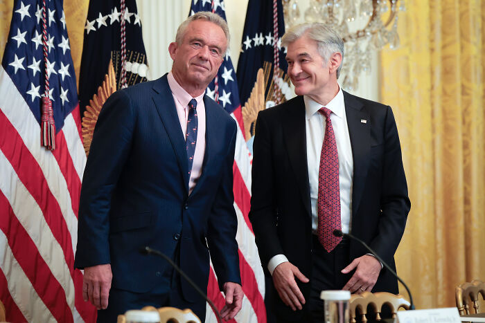 Two men in suits stand before American flags during a government event after brutal government shutdown advice. Two men in suits stand before American flags during a government event after brutal government shutdown advice.