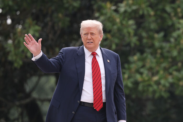 Former president Trump in a dark suit and red tie outdoors, related to Trump admin ballroom construction security necessity topic. Former president Trump in a dark suit and red tie outdoors, related to Trump admin ballroom construction security necessity topic.