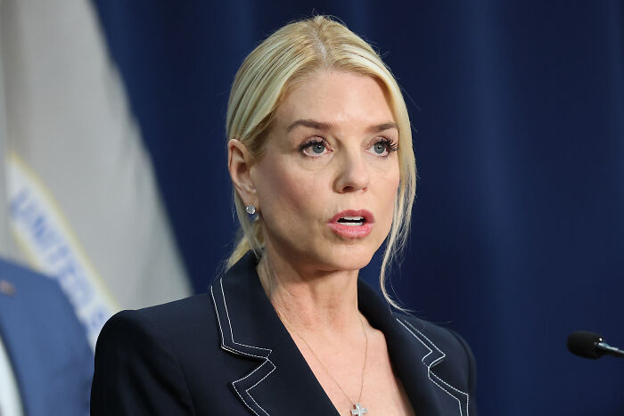 Pam Bondi speaking at a press conference, wearing a dark blazer, captured during a serious moment. Pam Bondi speaking at a press conference, wearing a dark blazer, captured during a serious moment.