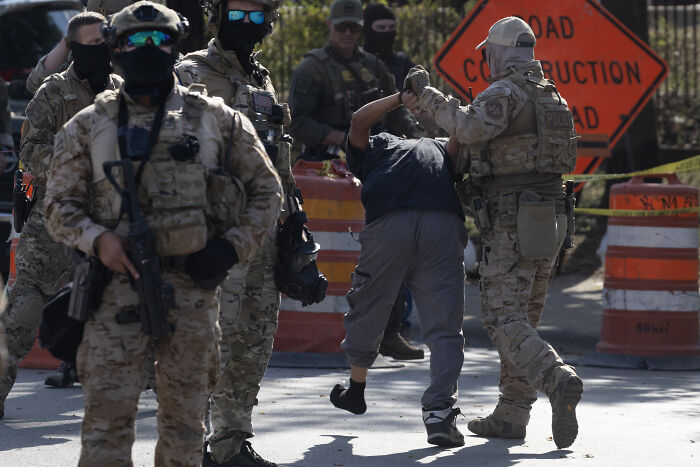 ICE agents in tactical gear detaining a person during raids, highlighting arrests with few convicted criminals involved.