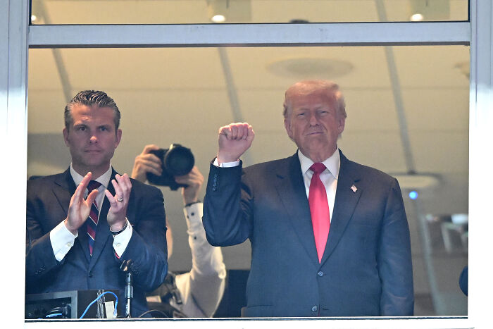 Trump raising fist beside a man clapping, revealing how he might throw Hegseth under the bus over war crime scandal.