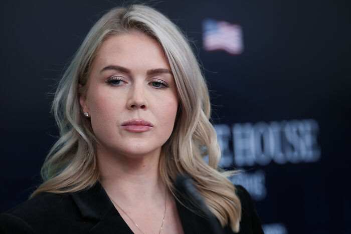 Karoline Leavitt at a press event, looking serious while addressing issues related to detained family and ICE custody.