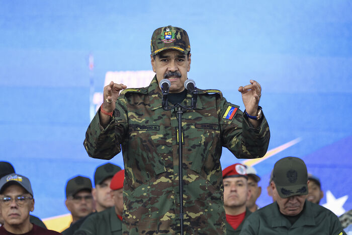 A military figure in camouflage speaks at a podium with microphones, highlighted in discussions on Trump’s war crimes Caribbean. A military figure in camouflage speaks at a podium with microphones, highlighted in discussions on Trump’s war crimes Caribbean.