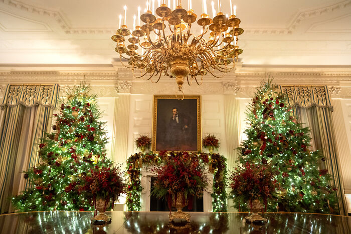 Elegant Christmas decorations with lush greenery and red accents in a grand room for Melania Trump’s 2025 holiday display.