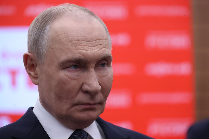 Close-up of a serious man in a suit against a red background representing terrifying events closer to WW3 in 2025.