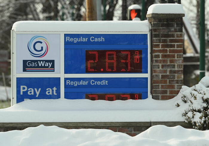 Gas station price sign covered in snow showing regular cash and credit rates during winter conditions. Gas station price sign covered in snow showing regular cash and credit rates during winter conditions.