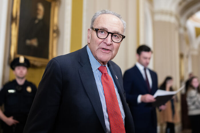 Man in glasses and red tie speaking indoors with uniformed officers and people in the background, relating to U.S. military d**g boat strikes. Man in glasses and red tie speaking indoors with uniformed officers and people in the background, relating to U.S. military d**g boat strikes.