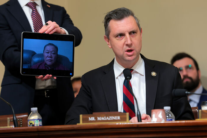 Congressman speaking at a hearing with a tablet showing a deported veteran joining remotely during veteran deportation testimony. Congressman speaking at a hearing with a tablet showing a deported veteran joining remotely during veteran deportation testimony.
