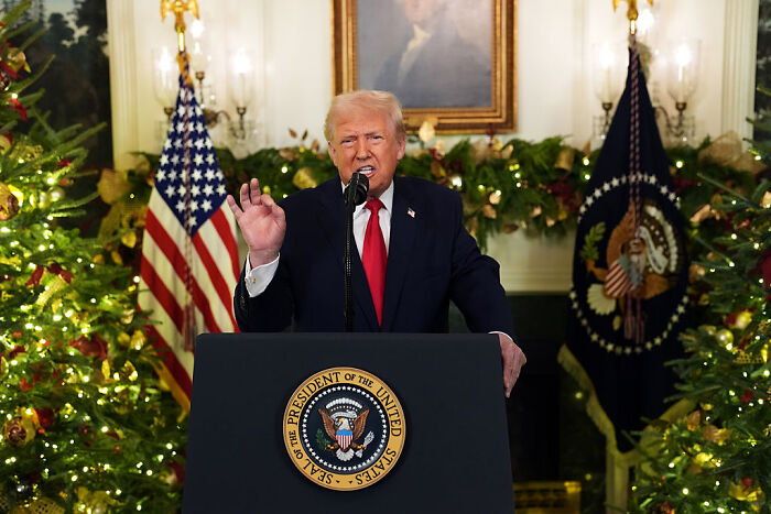 Donald Trump speaking on prime-time TV, standing at presidential podium with flags and Christmas decorations. Donald Trump speaking on prime-time TV, standing at presidential podium with flags and Christmas decorations.
