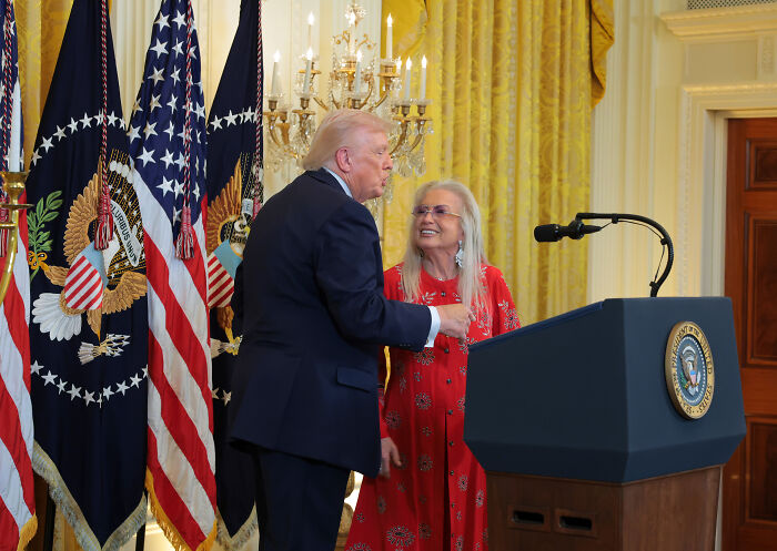Former President Trump speaking at a podium with US flags behind him, related to billionaire donor offer. Former President Trump speaking at a podium with US flags behind him, related to billionaire donor offer.