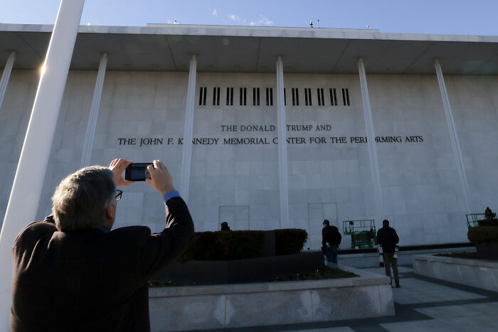 Man taking photo of the Trump Kennedy Center exterior, referencing Trump&rsquo;s Kennedy Center website hijacked comedic incident.