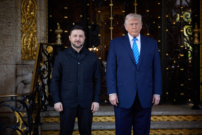 Volodymyr Zelenskyy and Donald Trump standing side by side, with discoloration visible on Trump&rsquo;s left hand.