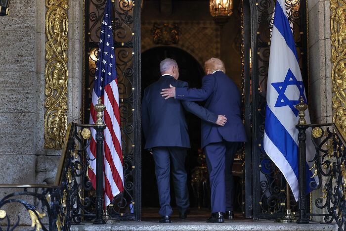 Two men walking into ornate building entrance with US and Israeli flags, illustrating Iran warns severe response after strike threats. Two men walking into ornate building entrance with US and Israeli flags, illustrating Iran warns severe response after strike threats.