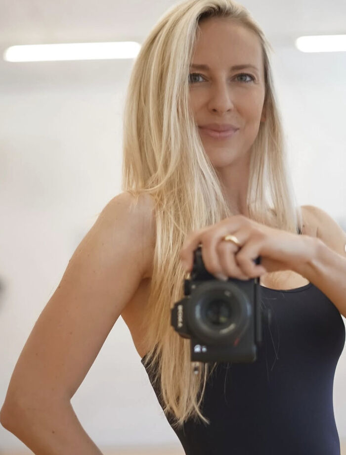Blonde woman in black top holding a camera, related to husband charged case involving Miss Switzerland finalist wife. Blonde woman in black top holding a camera, related to husband charged case involving Miss Switzerland finalist wife.