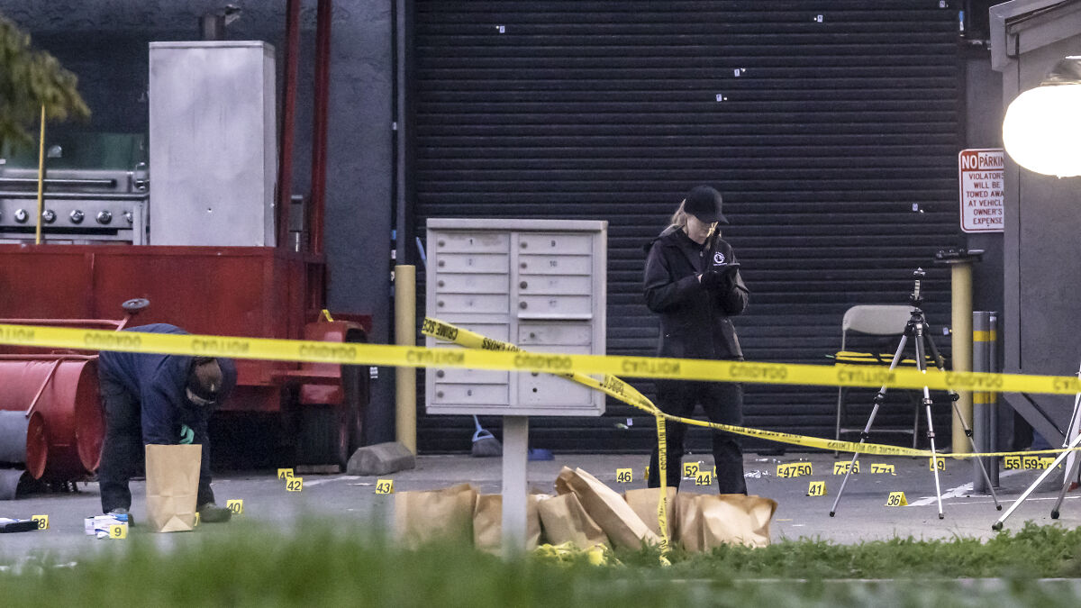 Crime scene investigators collecting evidence behind yellow caution tape at California location after gunman incident.