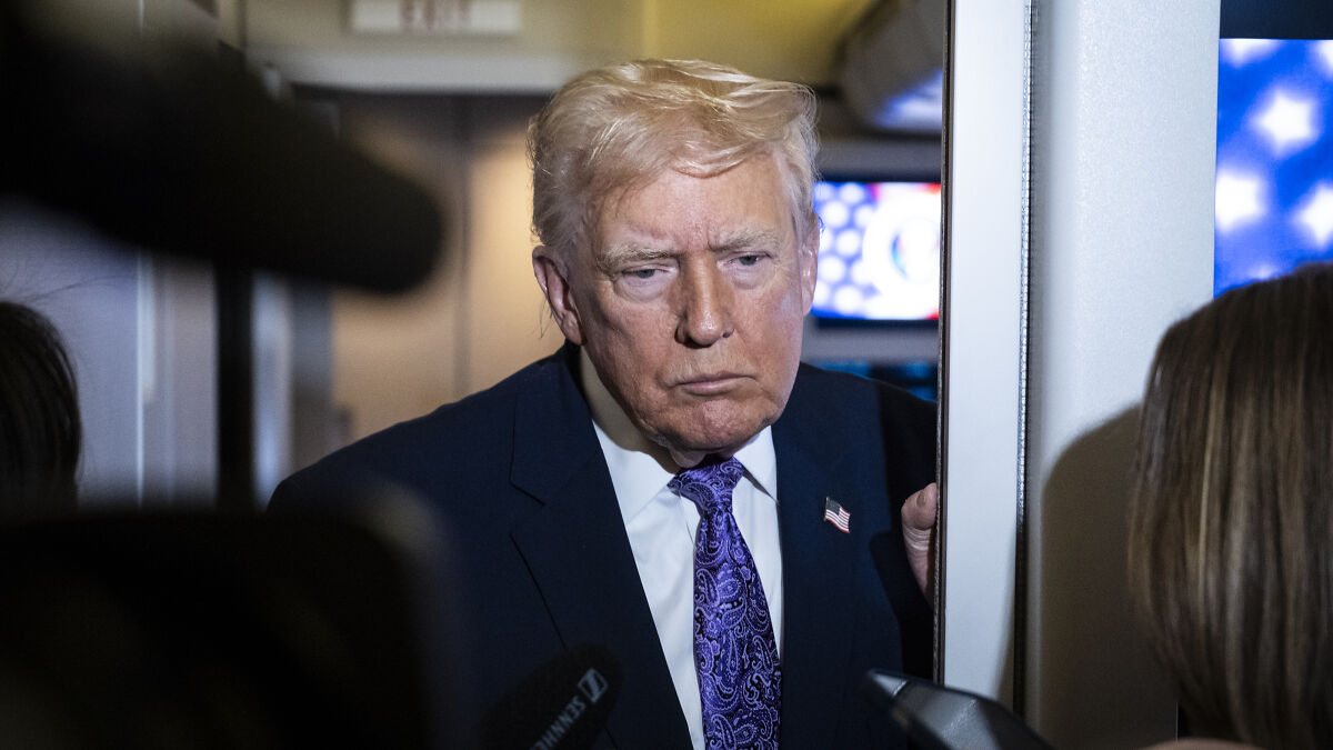 Donald Trump speaking to press, wearing suit and paisley tie, amid war crime scandal and Hegseth controversy.