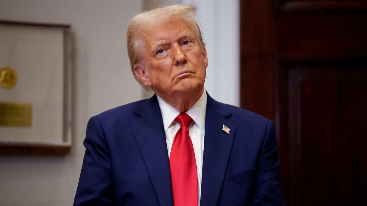 Donald Trump in a navy suit and red tie, standing indoors with a serious expression, related to Trumpu2019s nephew controversy.