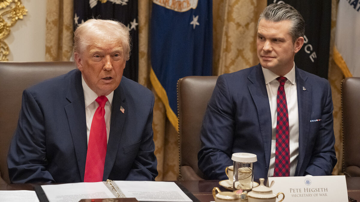 Two men in suits seated at a table during a discussion about Newsom reminding Hegseth of boat strike scandal consequences.