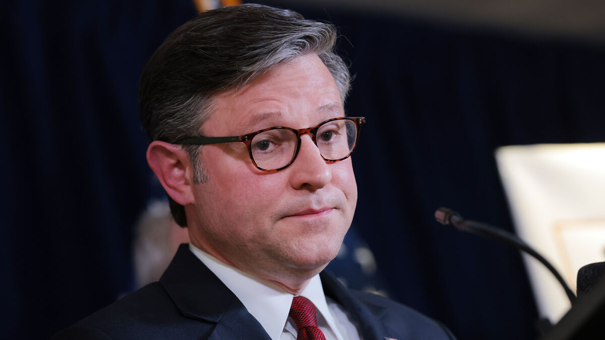 House Speaker Mike Johnson speaking at a podium with a serious expression during a political event.