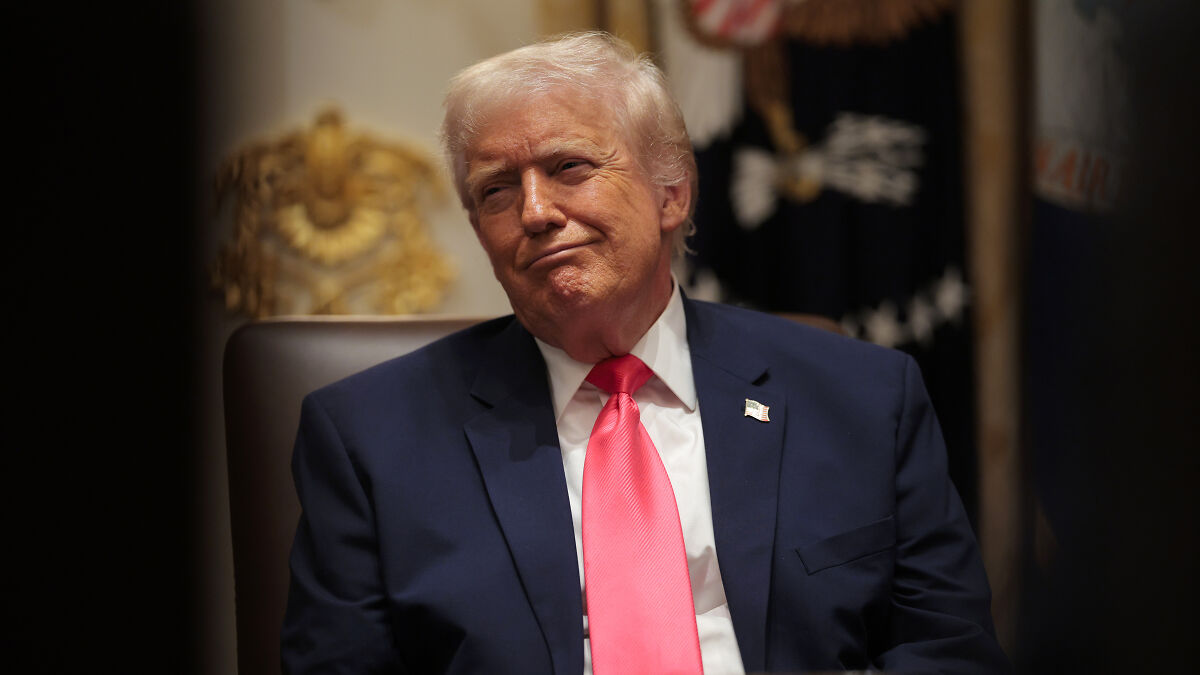 Donald Trump in a suit and bright pink tie, expressing a smirk while sitting indoors, linked to Kennedy Center renaming.