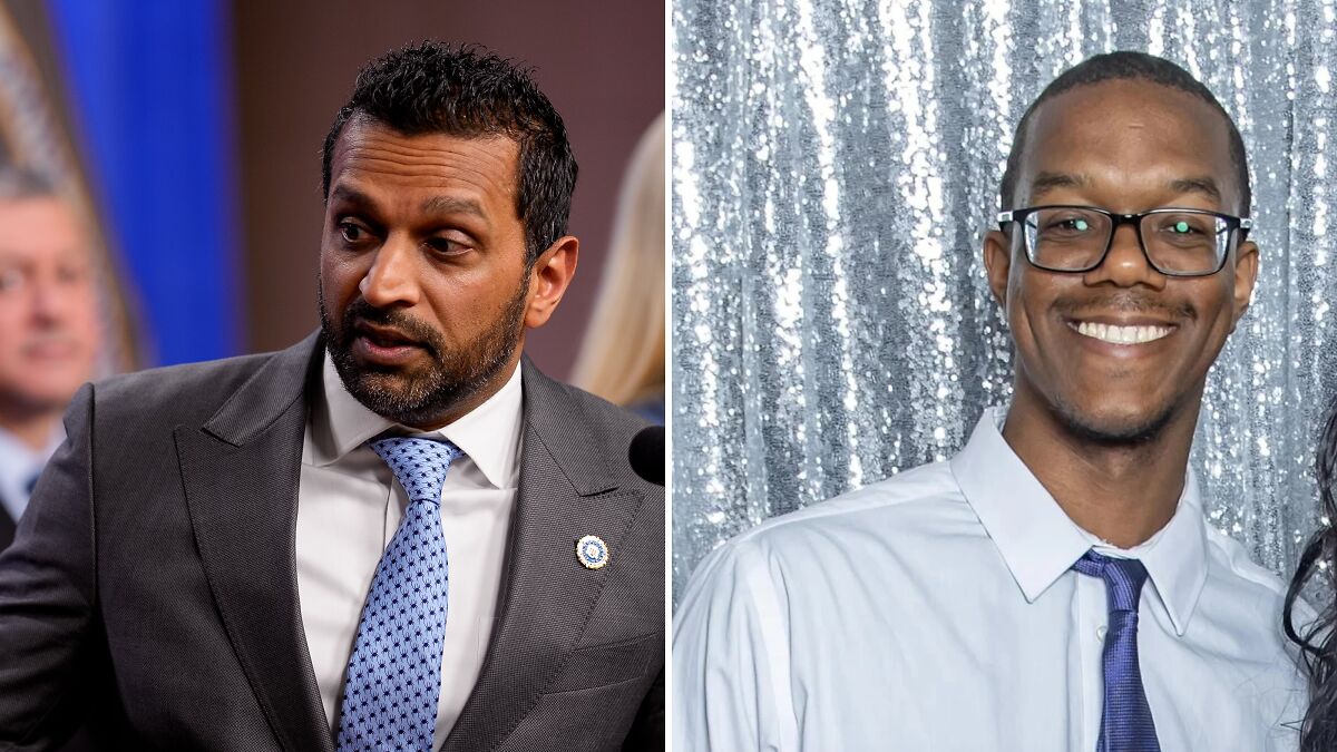 Man in gray suit and patterned tie speaking at an event alongside a smiling man in glasses and white shirt with blue tie