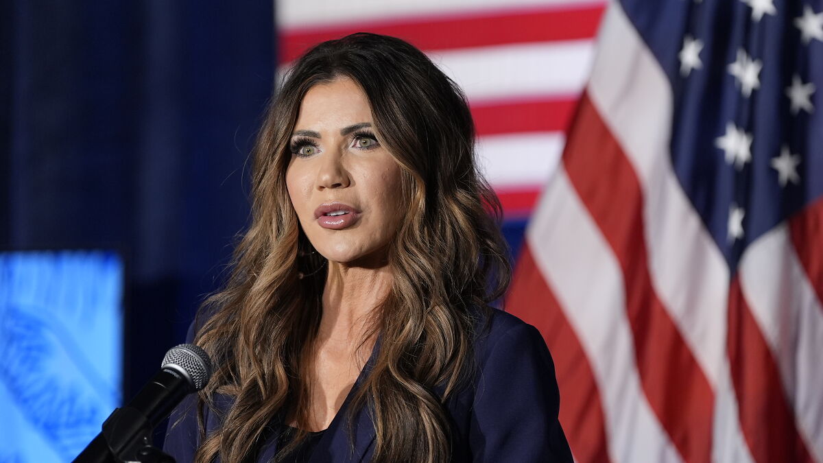 Kristi Noem speaking at event with American flags in background during hot mic moment involving TSA staff fear.